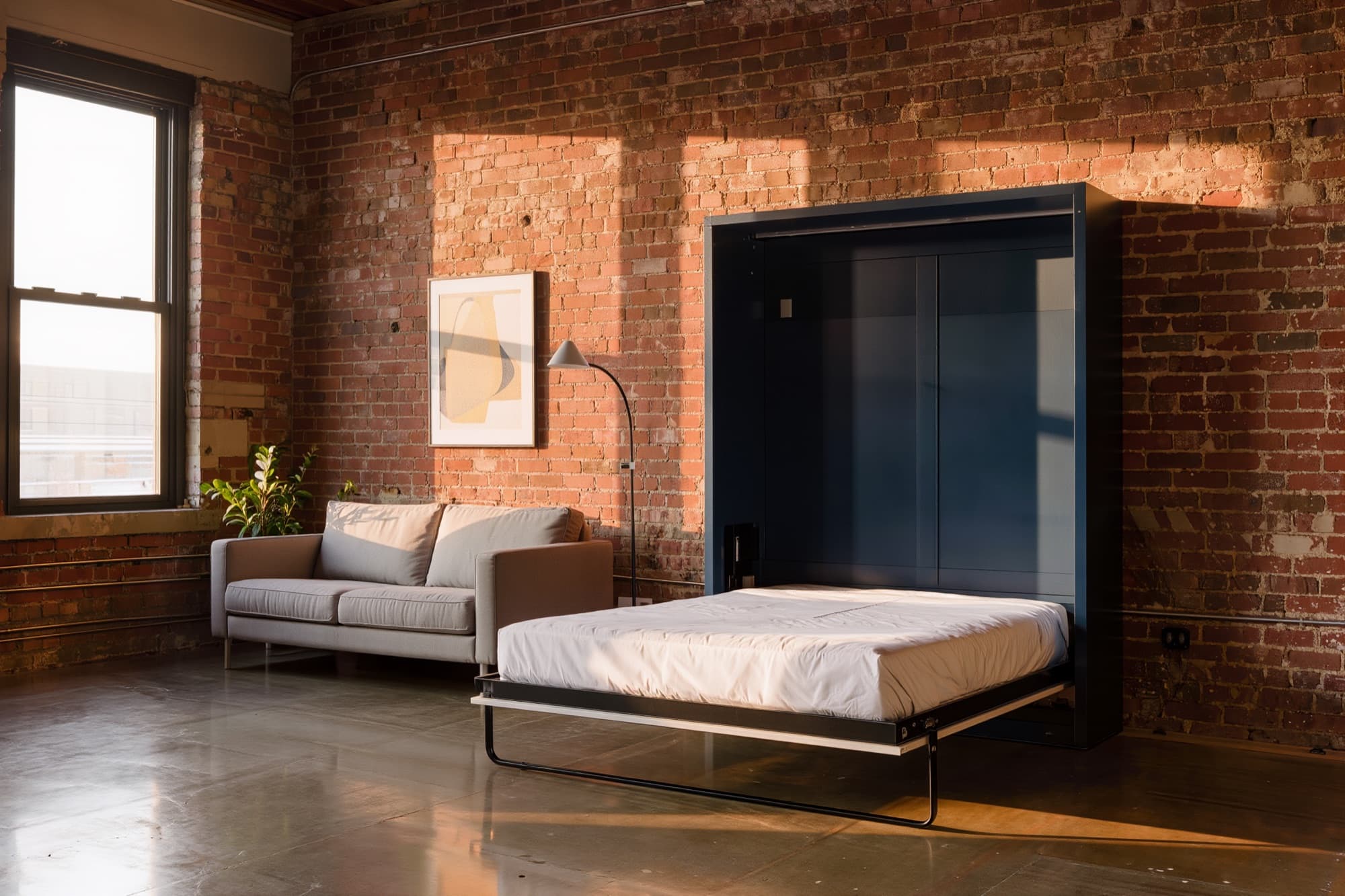Navy murphy bed folded down beside a sofa in a brick loft apartment